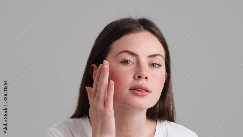 A close-up view of a pleased woman wearing basic T-shirt is looking to the camera as to the mirror standing isolated over grey background in the studio A close-up view of a pleased woman wearing basic T-shirt is looking to the camera as to the mirror standing isolated over grey background in the studio