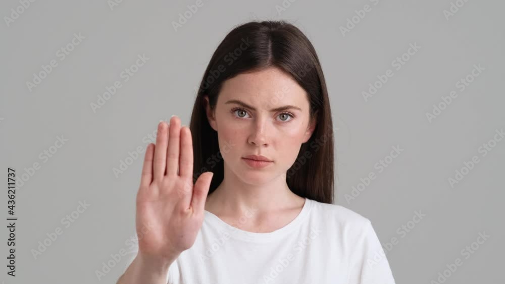A close-up view of a serious woman is showing stop gesture standing isolated over grey background in the studio A close-up view of a serious woman is showing stop gesture standing isolated over grey background in the studio