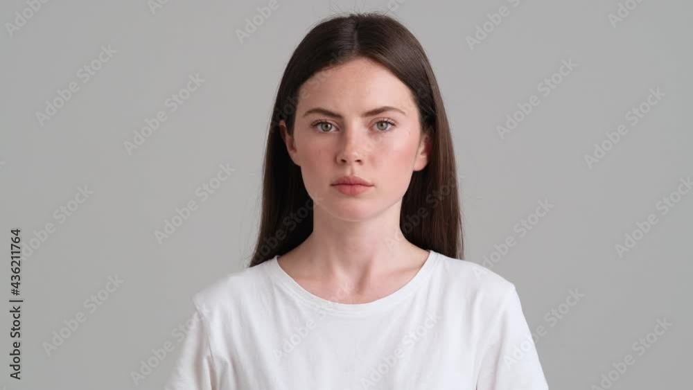 A close-up view of a serious woman is giving negative answer standing isolated over grey background in the studio A close-up view of a serious woman is giving negative answer standing isolated over grey background in the studio