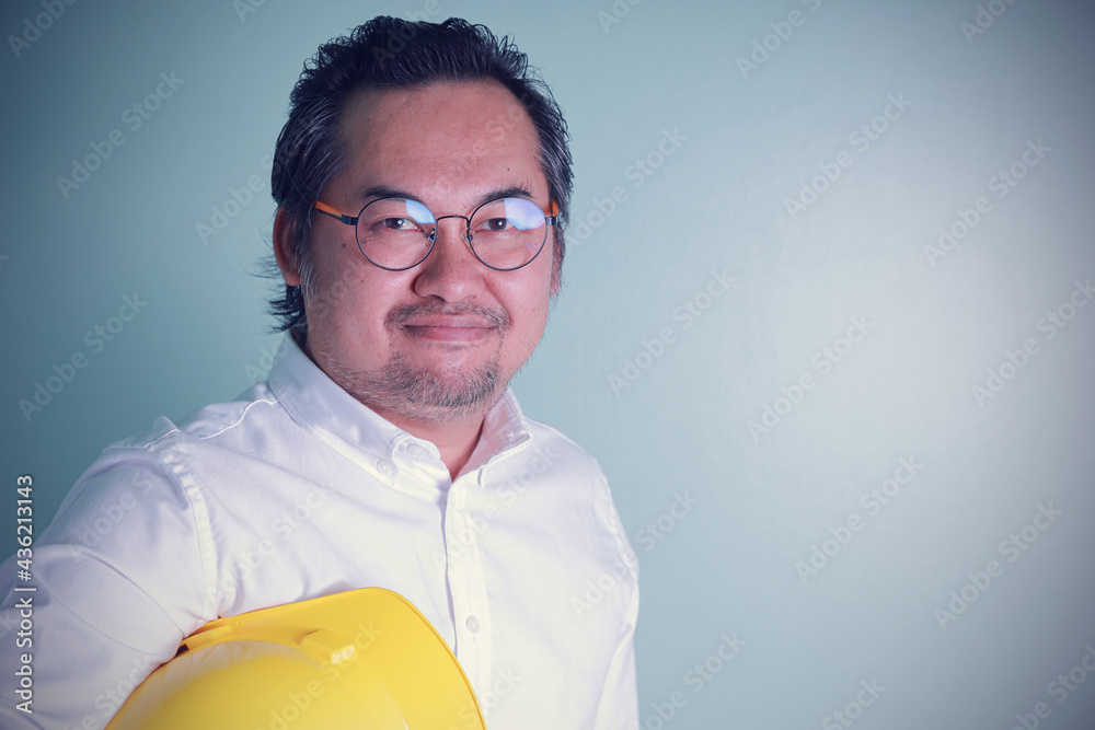 Portrait Asian businessman adult wearing glasses holding hard yellow hat smile happily looking at the camera. Professional handsome engineering leadership positive on the job for target success.