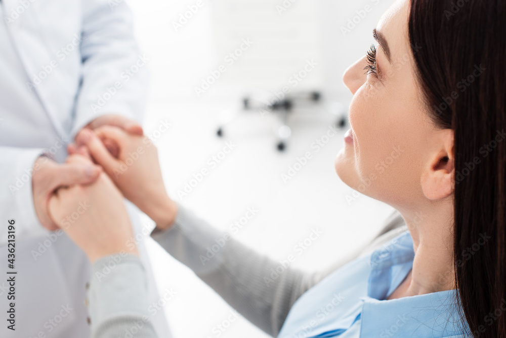 Fototapeta premium smiling woman holding hands of doctor in white coat in dental clinic.