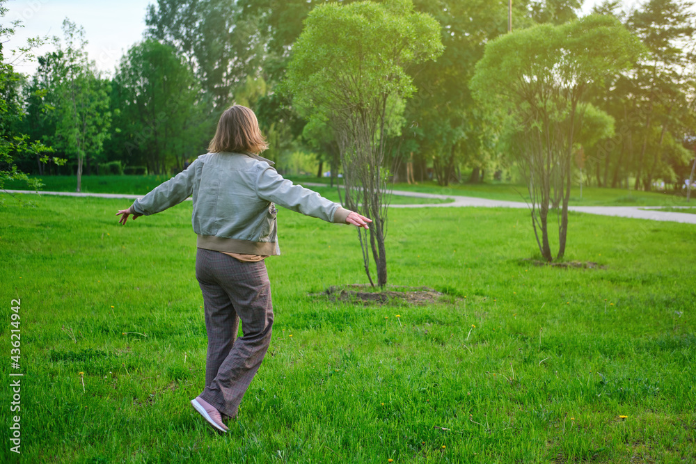 A woman in casual clothes dancing on the grass, relaxing on the park lawn A woman in casual clothes dancing on the grass, relaxing on the park lawn