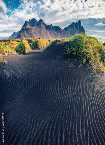 Spectacular summer view of Stokksnes cape with Vestrahorn (Batman Mountain) on background. Incredible Icelandic landscape with black sand dunes with fresh green grass on top.