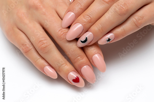 Delicate manicure. Beige, natural manicure with a painted black moon, stars and a red heart on long oval nails close-up on a white background.