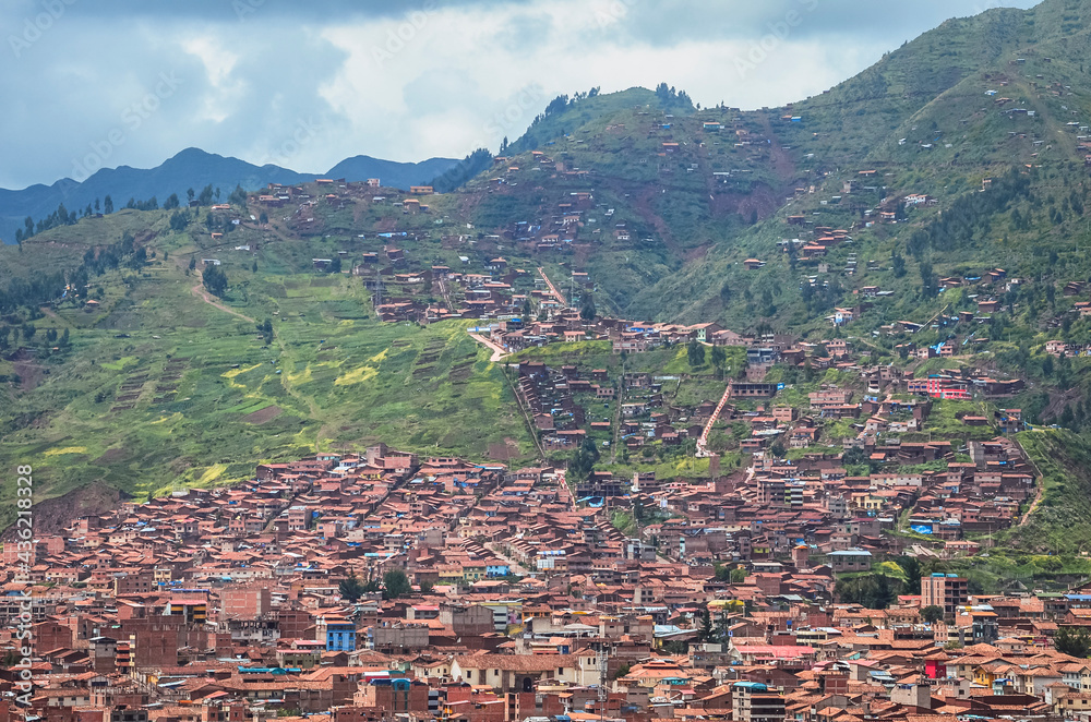 Aerial view of rooftops in Cusco city with the valley surrounded by green fields and the sky in the bottom. Houses and churches from a fair away point. Peru, South America