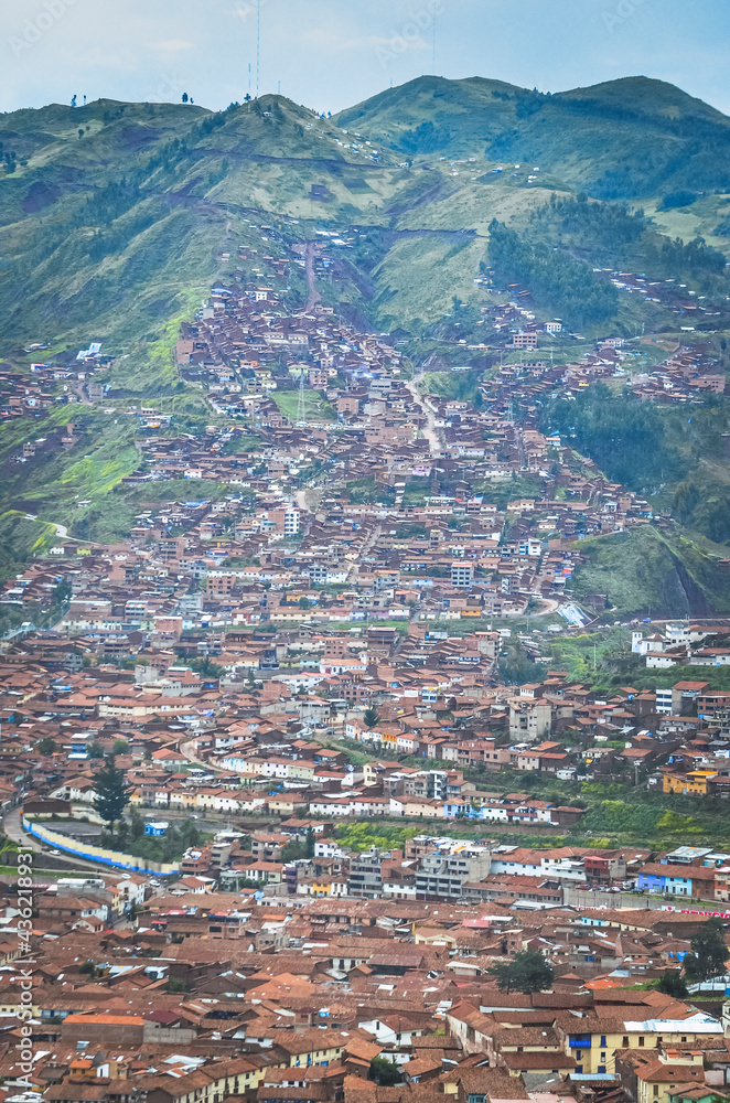 Aerial view of rooftops in Cusco city with the valley surrounded by green in the bottom. Houses and churches from a fair away point. Peru, South America