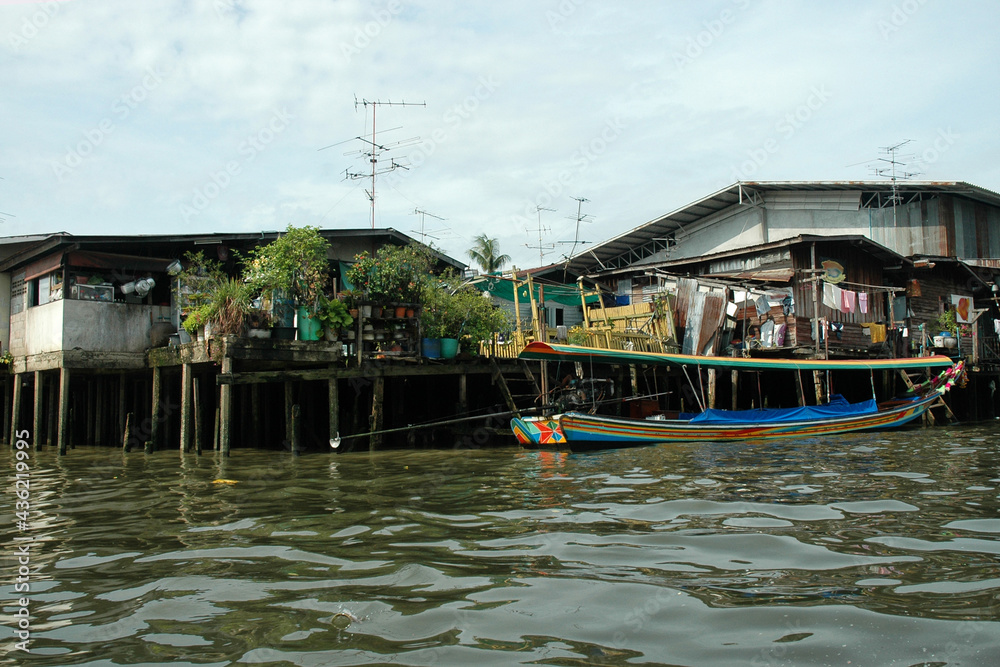 Stilt slum housing in Bangkok with boat used for touring in foreground