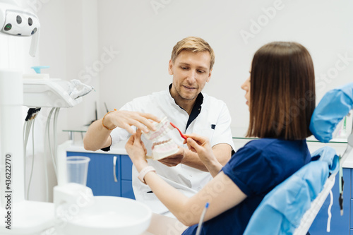 Dentist showing the correct dental hygiene using mock-up of skeleton of teeth. Stomatologist doctor explaining proper dental hygiene to patient holding sample of human jaw with toothbrush.