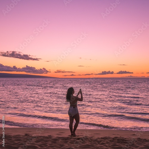 Woman in bikini taking photos of the sunset on her vacation in Hawaii