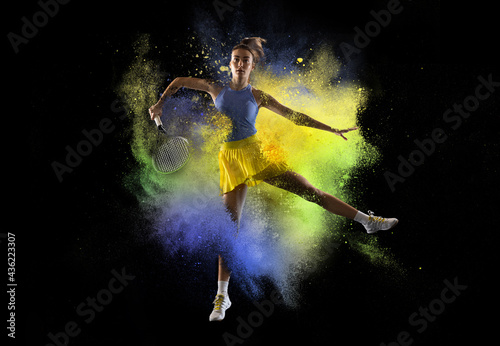 Young girl tennis player in explosion of colored neon powder isolated on dark background. Purple and yellow