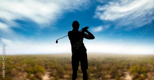 Composition of silhouette of male golf player over landscape and clouds on blue sky with copy space