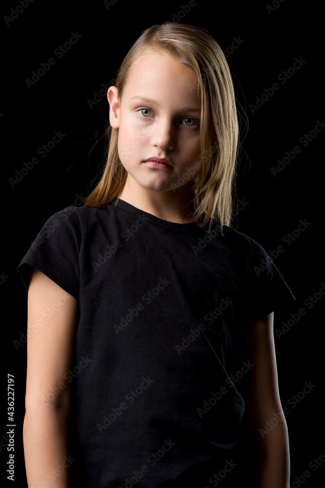 Close-up portrait of a beautiful blonde teenage girl in a black t-shirt on a black background.