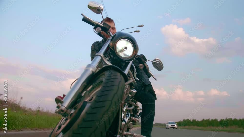 Young man sitting on motorcycle on the road at sunset, slow motion Young man sitting on motorcycle on the road at sunset, slow motion