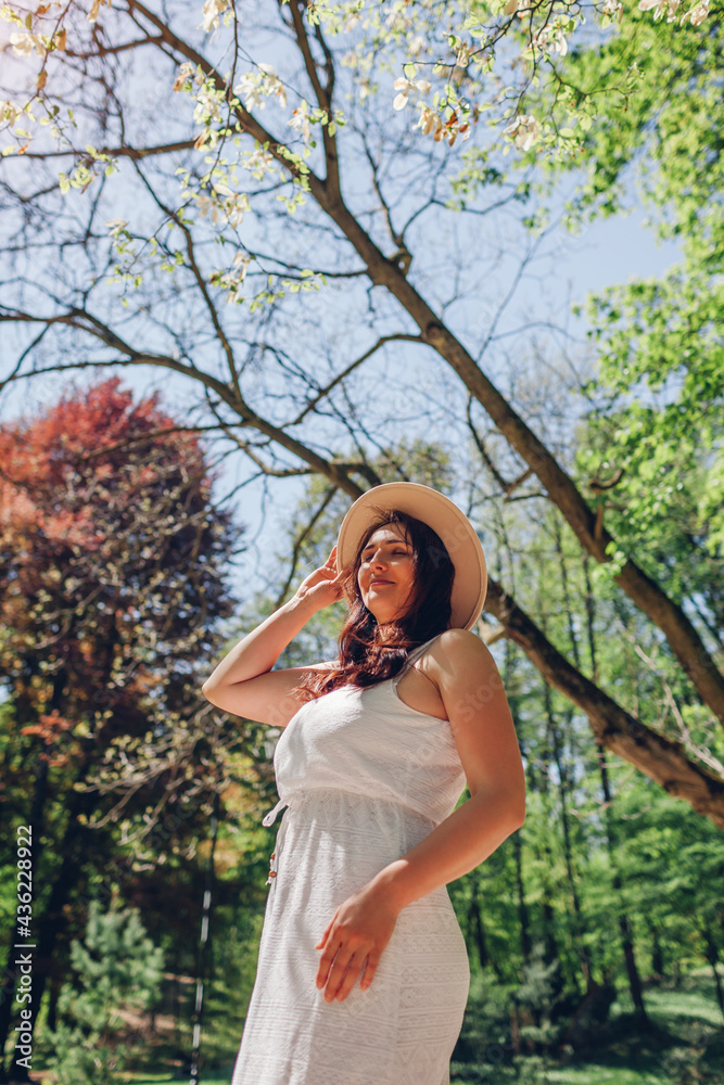 Portrait of middle-aged woman walking in blooming spring garden. Happy stylish lady wearing hat outdoors