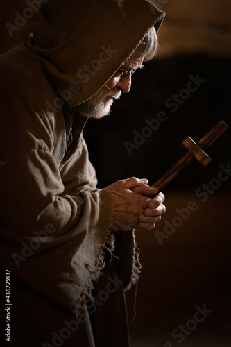 Old poor monk looks at the cross and doubts