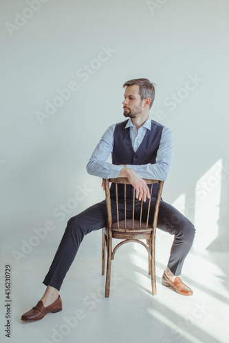 Portrait of a man in a shirt and waistcoat sitting and leaning on the back of a chair in sunlight