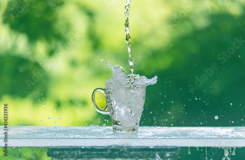 Water flows into a glass placed on a wooden bar,over sunlight and natural green background.blur shadow.