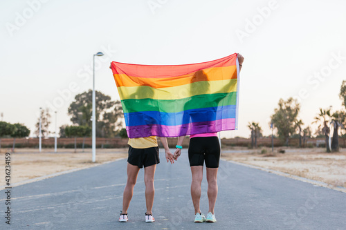 Beautiful sporty lesbian couple holding hands with the rainbow flag, equal rights for the lgbt community.