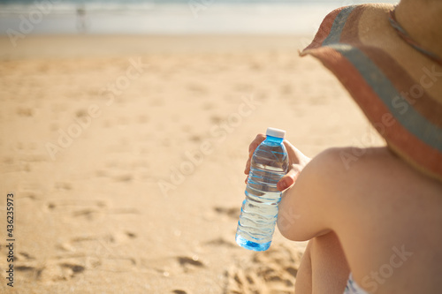 Side view of a girl on the beach holding a bottle of mineral water.