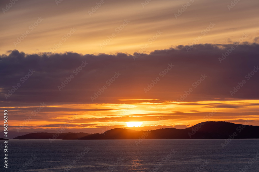 Obraz premium A beautiful pink sunset over the ocean with an island and mountains in the distance.