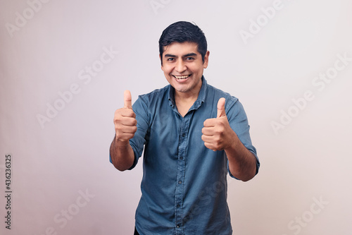 Hombre joven y feliz sonriendo en primer plano levanta pulgares. Modelo aislado en fondo blanco con camisa azul photo