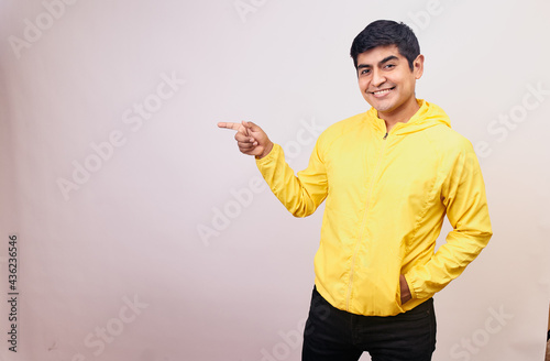 Hombre joven y feliz con una mascarilla señala con sus manos y dedos. Modelo aislado en fondo blanco con casaca amarilla