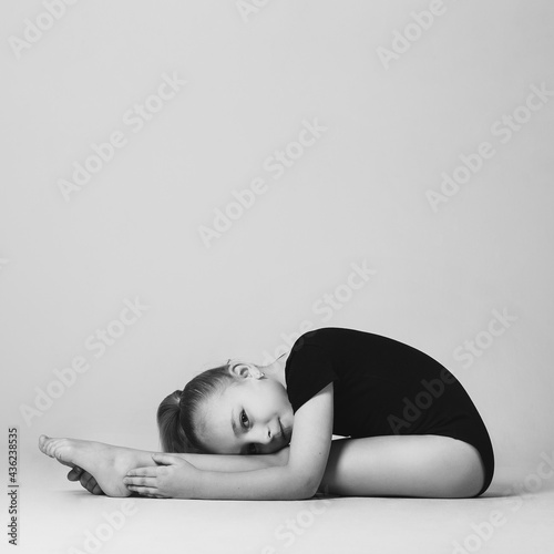 Girl gymnast doing bends to the legs, looking easily at the camera