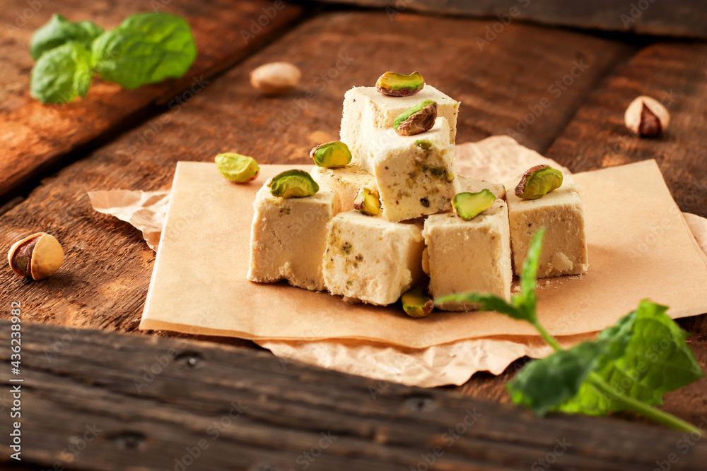 Walnut halva with pistachios on parchment paper on a wooden background. Traditional oriental dessert Chekme. Natural vegan sweets. Rustic style