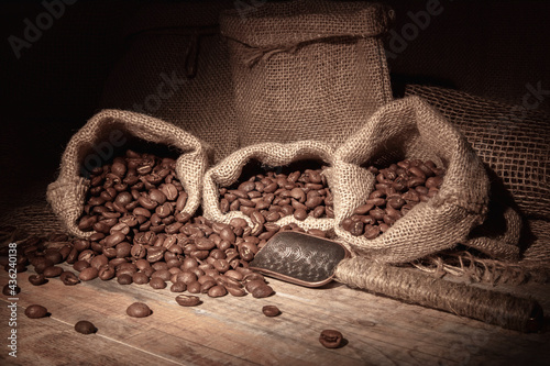 Vintage. Coffee beans in bags, scattered on a wooden table, illuminated by a beam of warm light. Spoon for coffee beans.