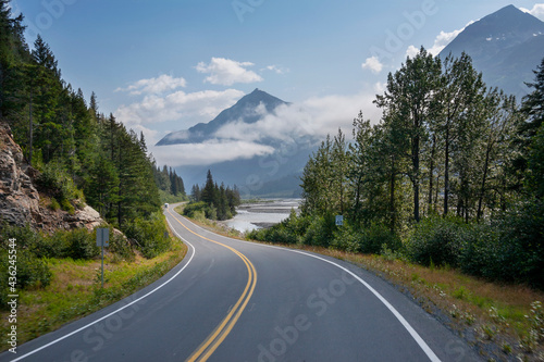 Camper travels along a curving highway in Alaska below mountains near Seward on a sunny afternoon