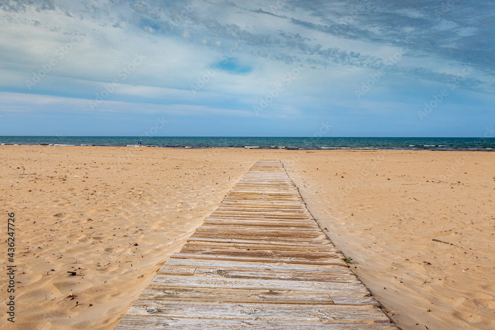 Wooden walkway extended on a fine sandy beach with the Mediterranean Sea in the background. In a cloudy sunset.