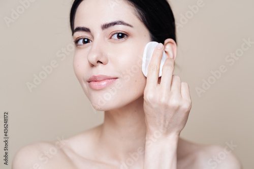 Canvas Print Beautiful Caucasian woman gently cleaning face with makeup remover pad ion beige