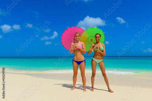 Girls having fun at the beach, standing on the seashore with pink and green umbrellas, interracial, black 