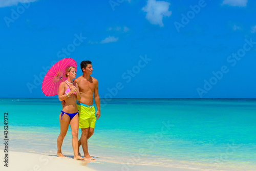 Couple walking on the seashore at the beach with pink umbrella