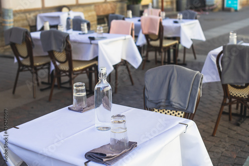 View of empty street cafe restaurant outdoor terrace veranda decoration on pedestrian european street, with chairs, tables decorated with white tablecoth, pink and grey blanket, bottles of water © tsuguliev
