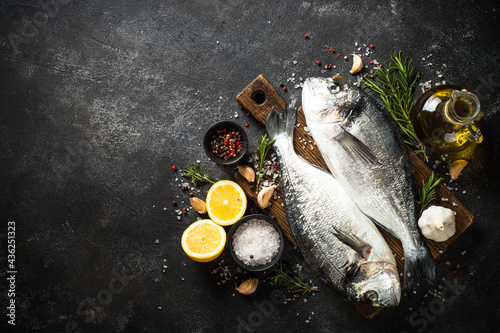Photography Fresh fish dorado on black stone table with ingredients for cooking