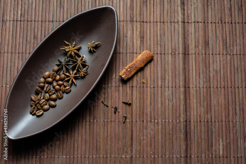 Brown canoe-shaped dish on bamboo mat with coffee beans, star anise, cloves and cinnamon