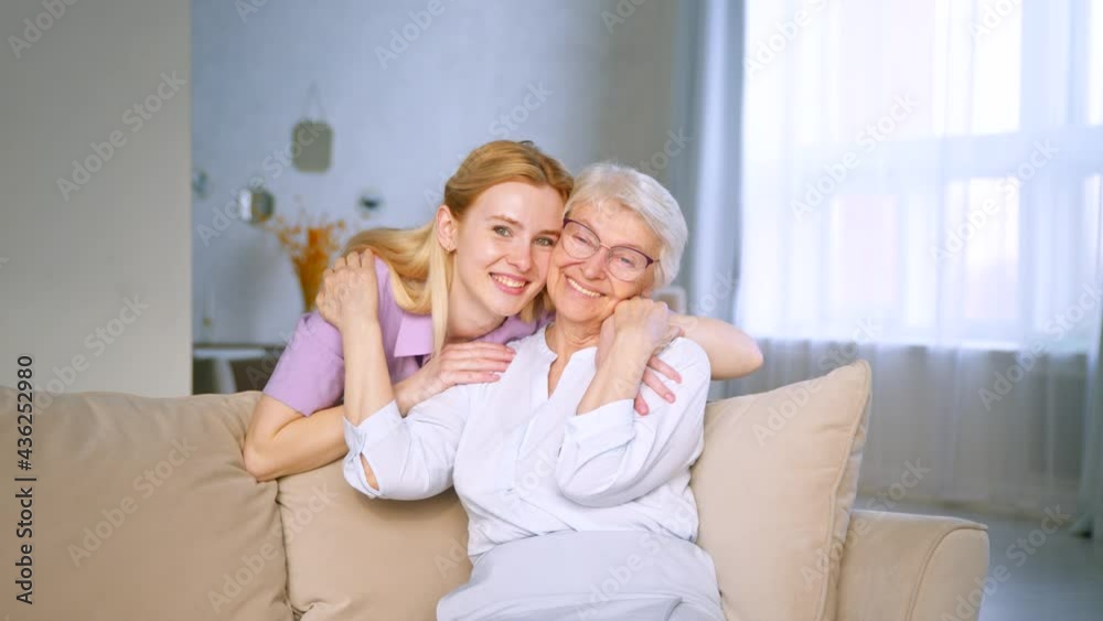 Young girl and elderly woman embracing on a couch. Smiling family looking at the camera with a smile