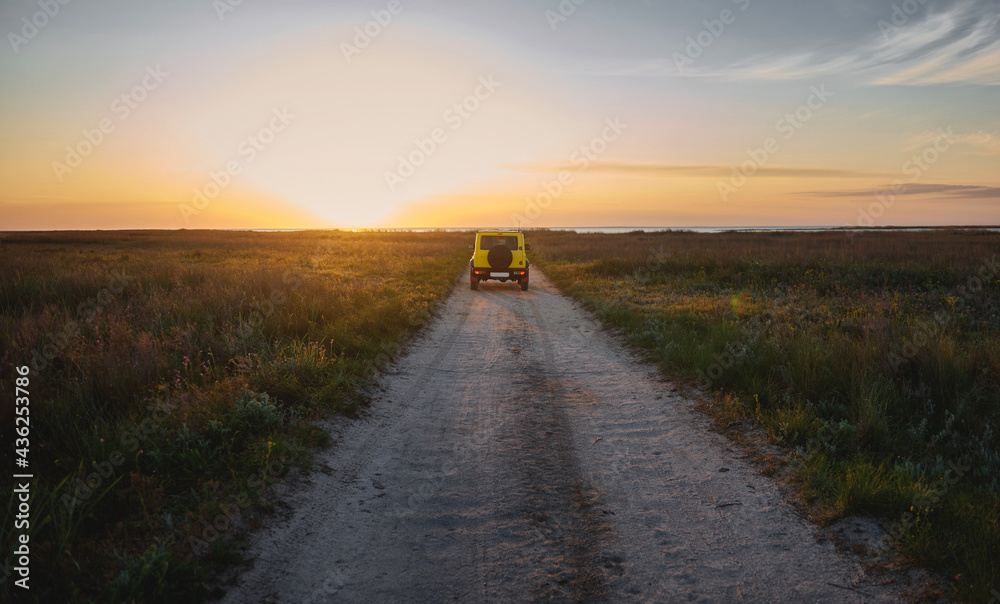 A car moving along a country steppe road in the light of a beautiful sunset sky A car moving along a country steppe road in the light of a beautiful sunset sky