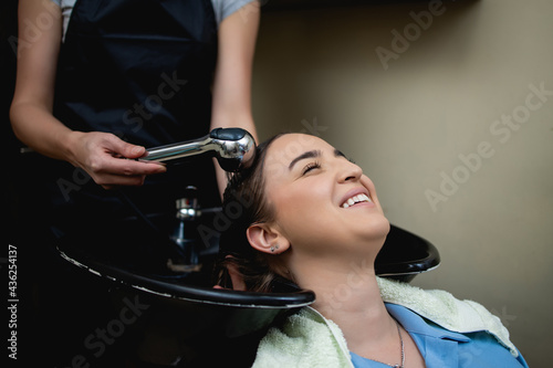 Hairdresser washing hair of a beautiful young adult woman in hair salon.