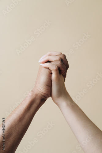 Multiethnic couple holding hands. Young Caucasian woman and African male arms together on beige background. Family Success concept