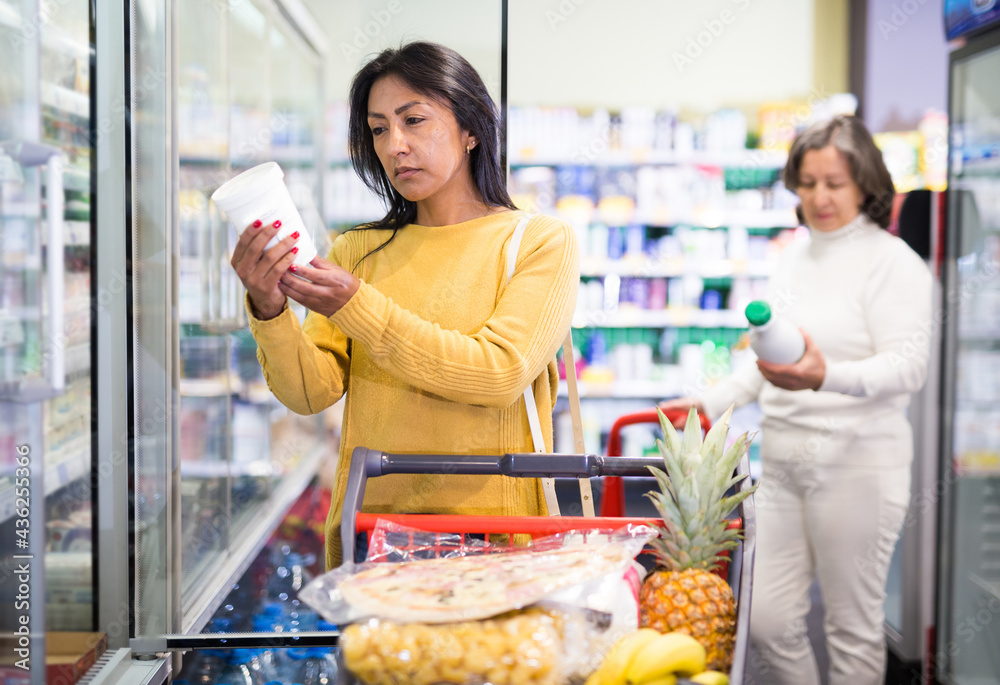 Female shopper pulls dairy products out of the refrigerator at a grocery supermarket