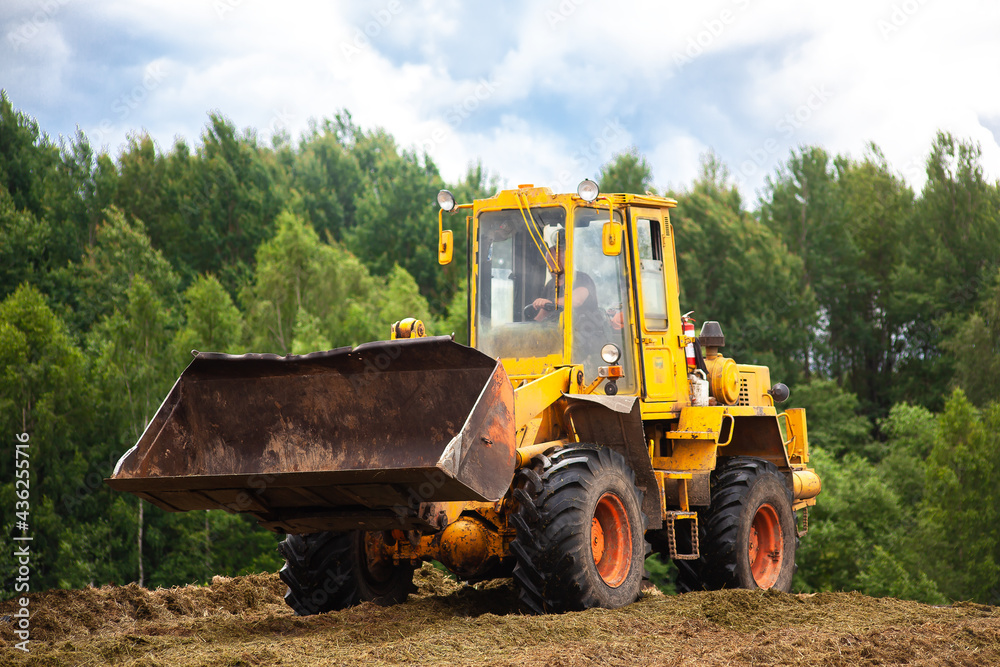 A yellow bulldozer is compacting a green mass of cut grass. A yellow bulldozer is compacting a green mass of cut grass.
