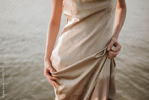 silhouette of a woman in a silk golden dress against the background of river water, beautiful folds of fabric