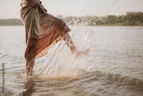 female feet and splashes of river water, a young woman in a golden dress plays on the shore at sunset