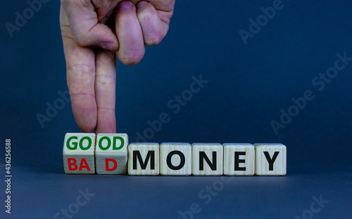 Good or bad money symbol. Businessman turns wooden cubes and changes words 'bad money' to 'good money'. Beautiful grey table, grey background, copy space. Business and good or bad money concept.