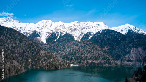 Aerial view of a lake surrounded by mountains with snow-capped peaks. Copy space.