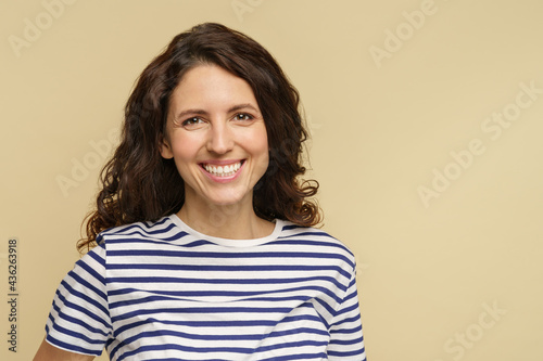 Closeup portrait of happy brunette woman with natural makeup, healthy skin and hair, stanning white toothy smile. Cheerful friendly millennial female in 30s over light beige studio wall background