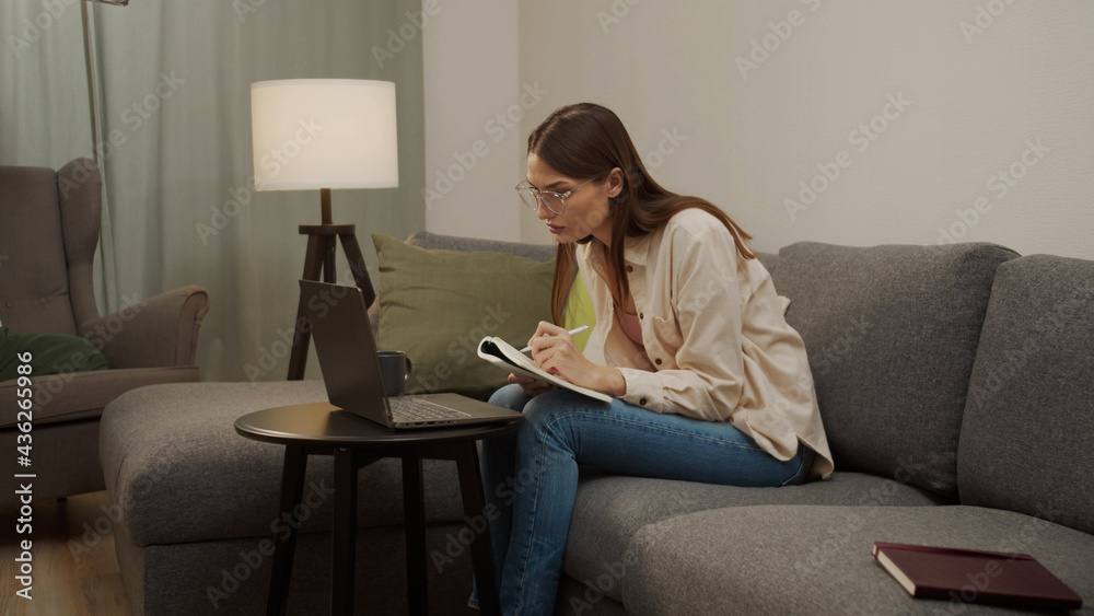 A european girl writes something in a notebook from a laptop A european girl writes something in a notebook from a laptop