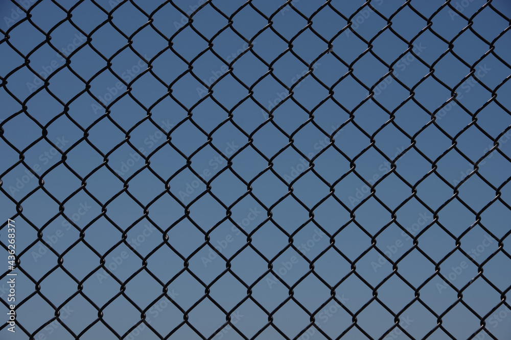 Full frame close-up view of a segment of a black chainlink fence with blue sky behind